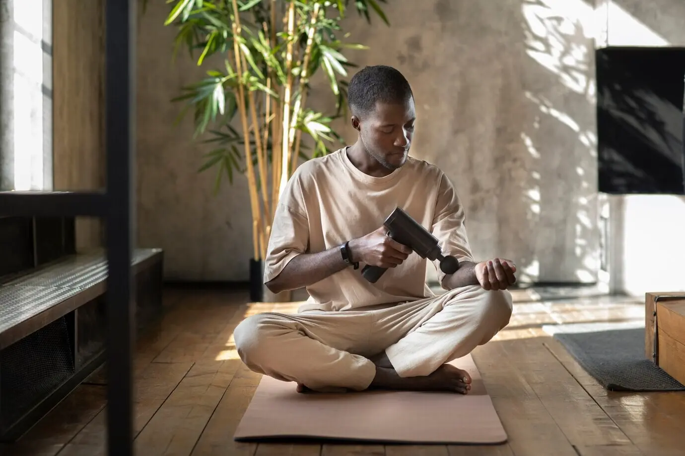 Full-body shot of a man using a massage gun on his arm.
